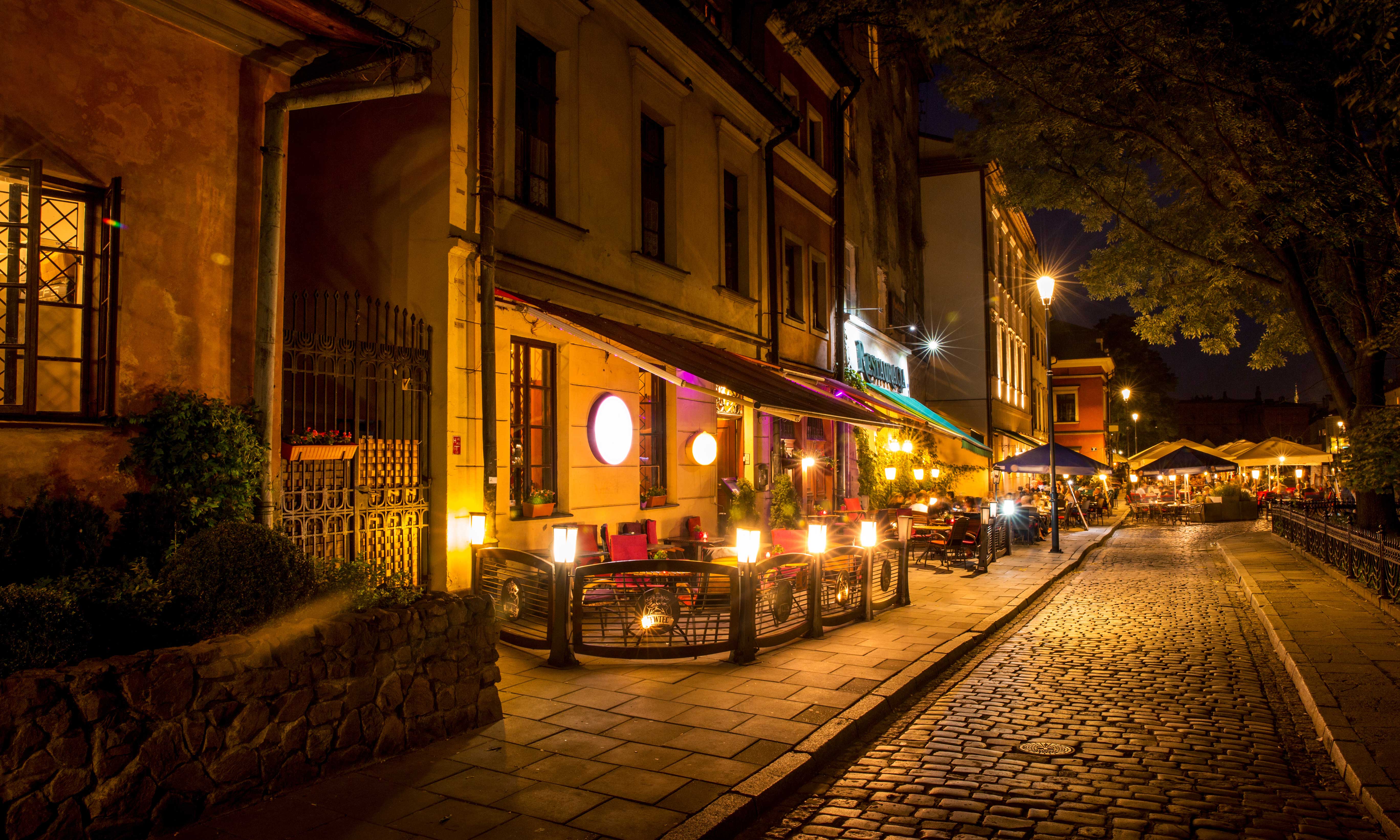 Night image of a street full of cafes and outside tables in Krakow, Poland.